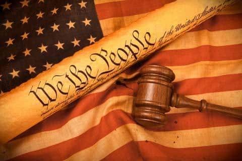 American flag, the constitution reading "we the people" and a brown wooden judges mallet